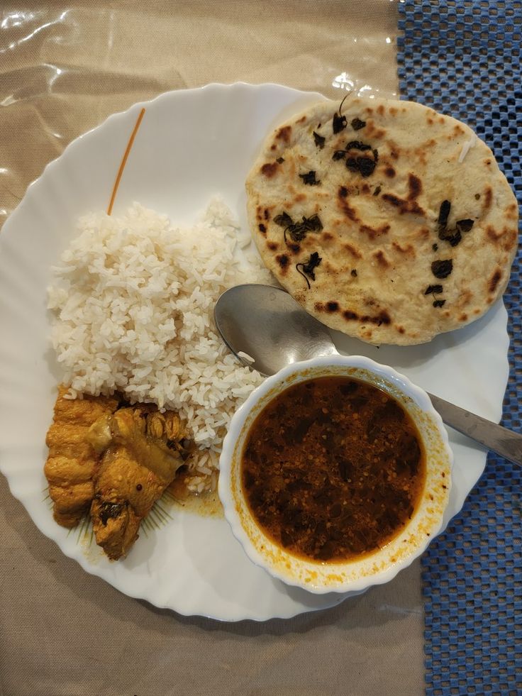 a white plate topped with rice and meat next to a bowl of sauce on top of a table