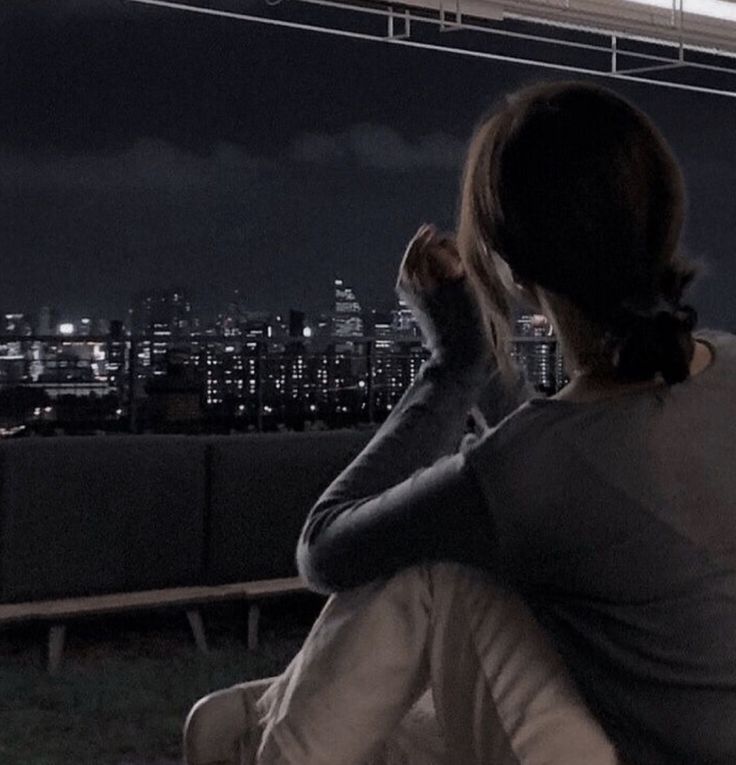 a woman sitting on top of a wooden bench in front of a cityscape