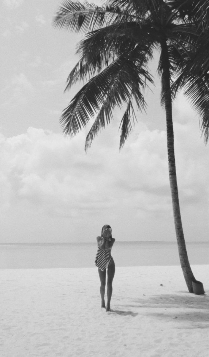 a woman standing on top of a sandy beach under a palm tree