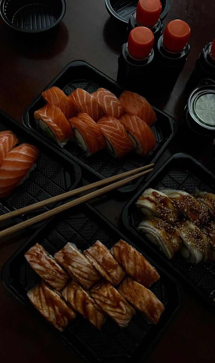 some sushi and chopsticks are sitting on trays next to each other