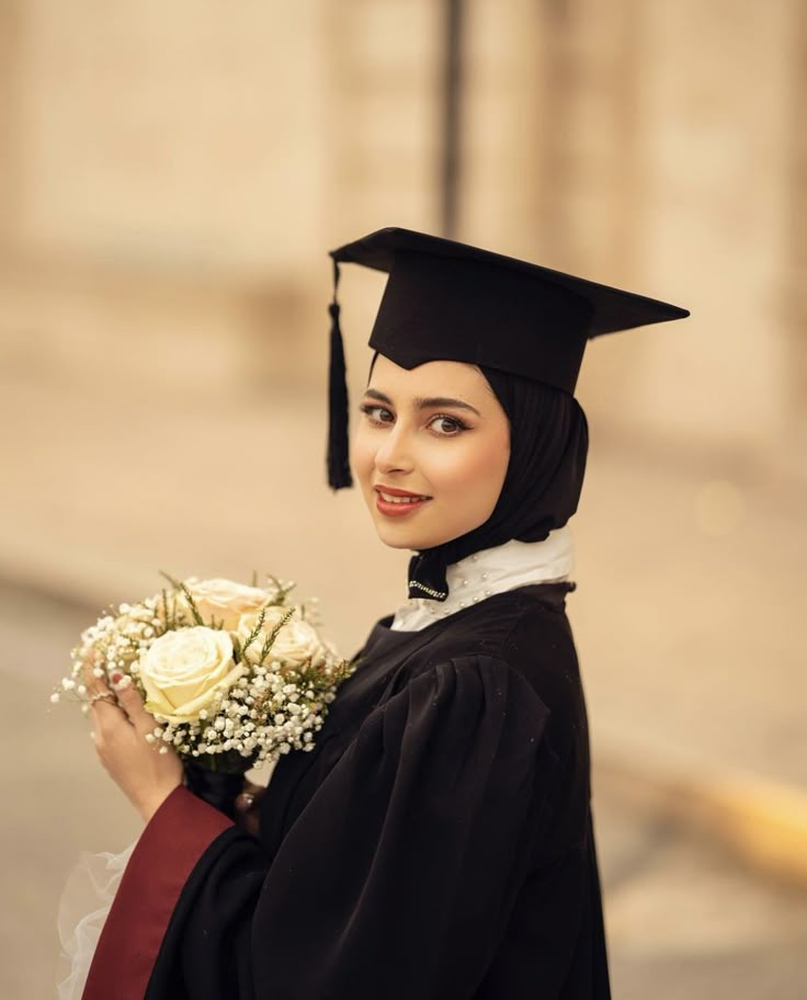 a woman wearing a graduation gown and holding a bouquet of flowers in her hand while standing on the street