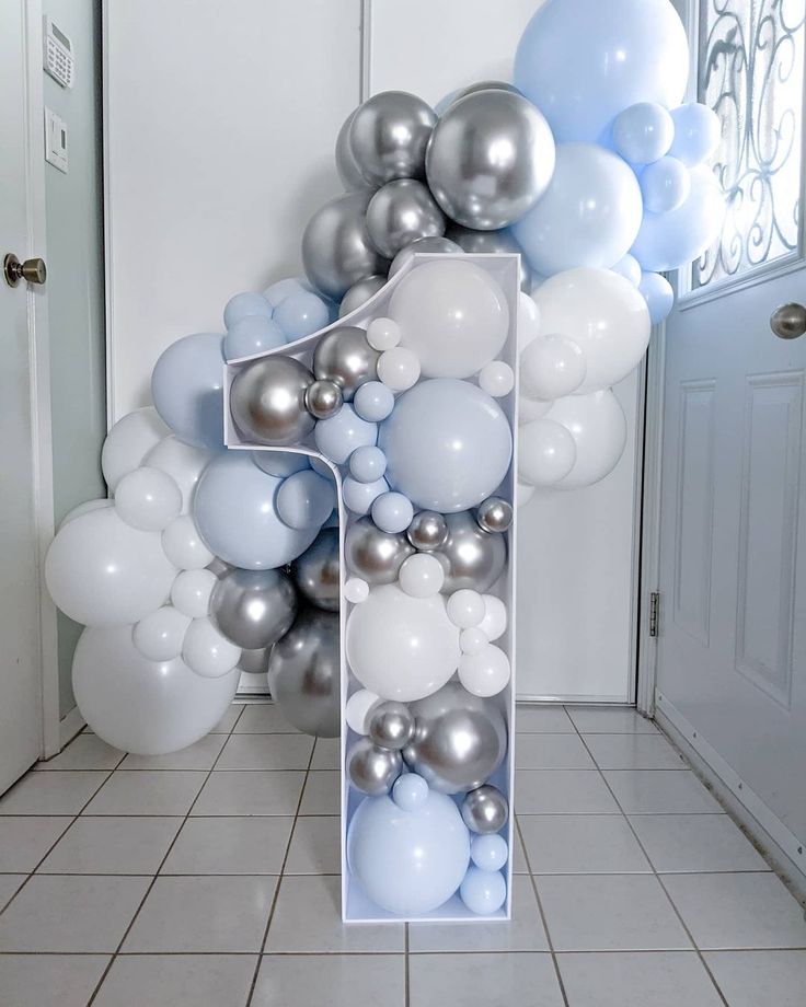 a number seven made out of balloons in front of a wall with white and silver balloons