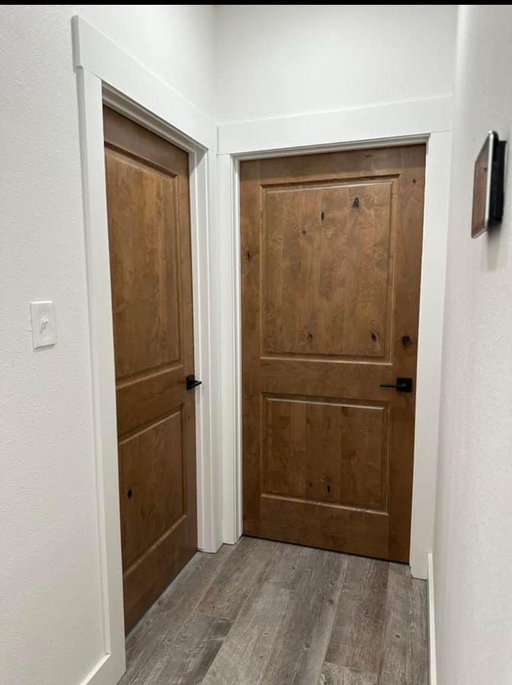 two wooden doors in a white room with wood flooring and gray walls on either side