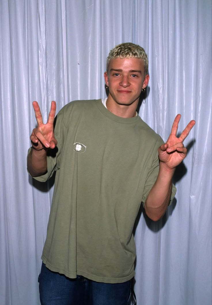 a man standing in front of a white curtain making the peace sign with his hands