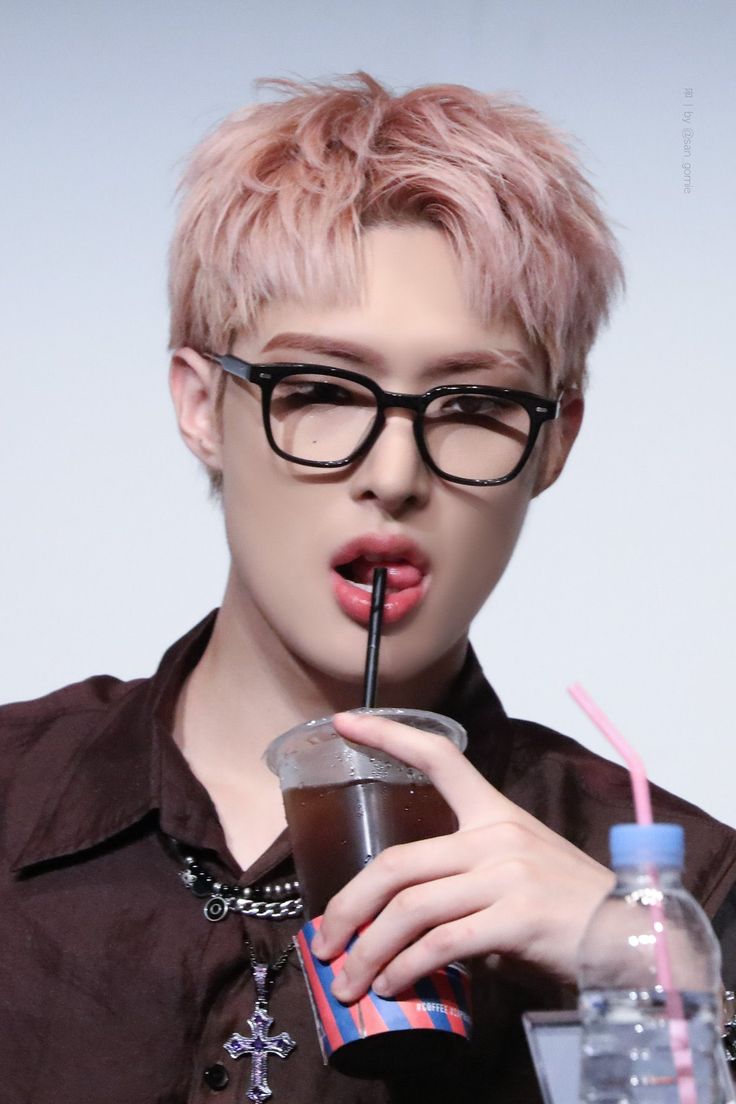 a person with pink hair and glasses drinking from a plastic cup while holding a straw