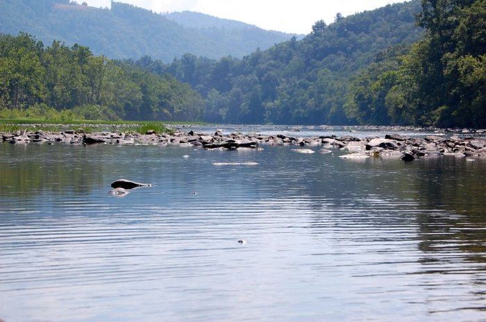 a body of water with rocks in it and mountains in the background on a sunny day