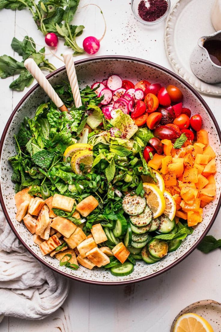 a bowl filled with salad and vegetables on top of a white table next to utensils