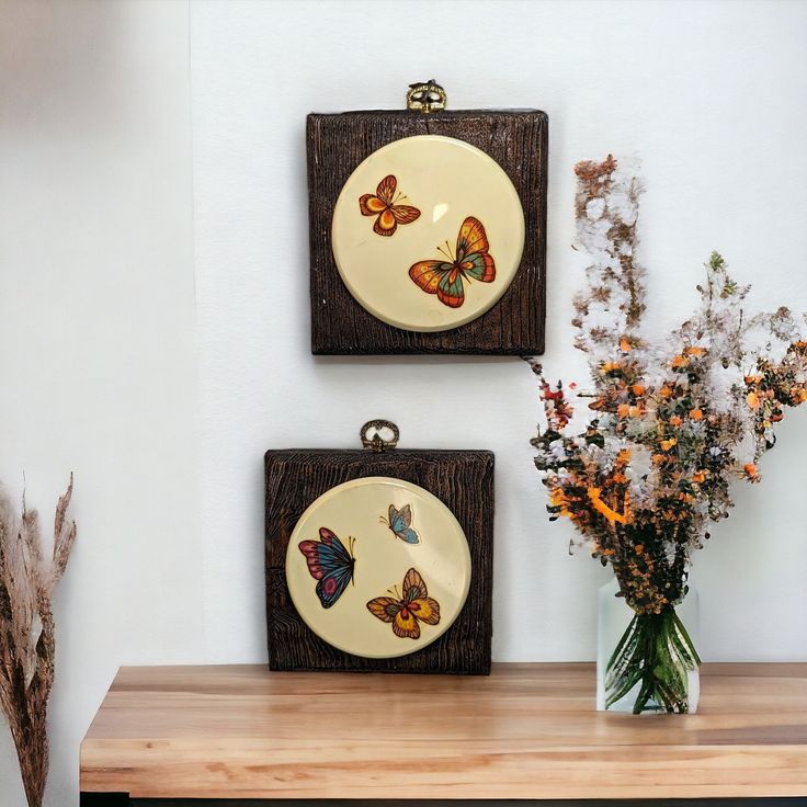 two butterflies are hanging on the wall next to a vase with flowers