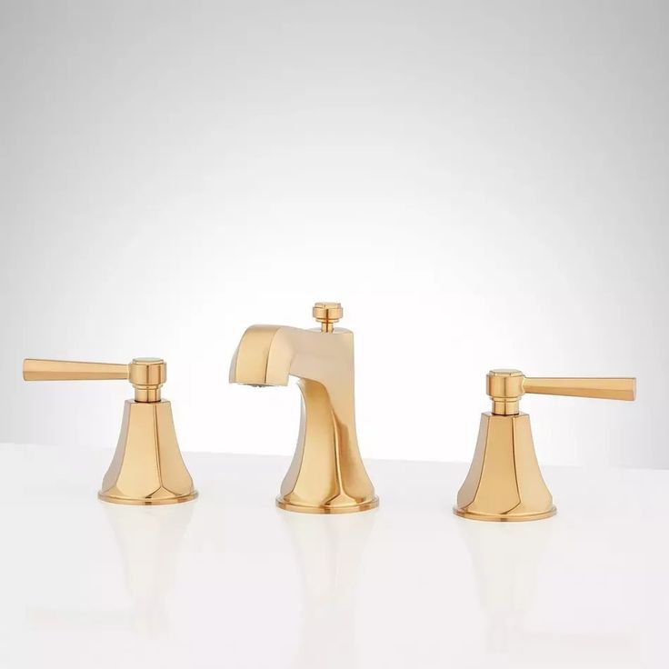 three golden faucets on a white surface