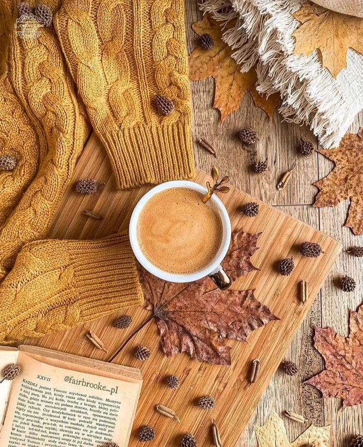 a cup of coffee sitting on top of a wooden table next to an open book