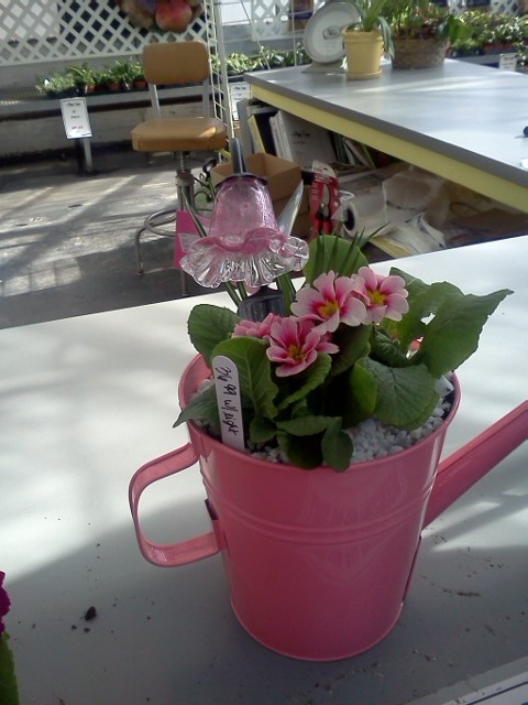 a pink watering can filled with flowers on top of a table