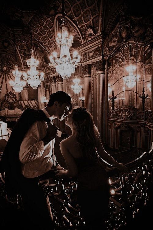 a man and woman kissing in front of chandelier