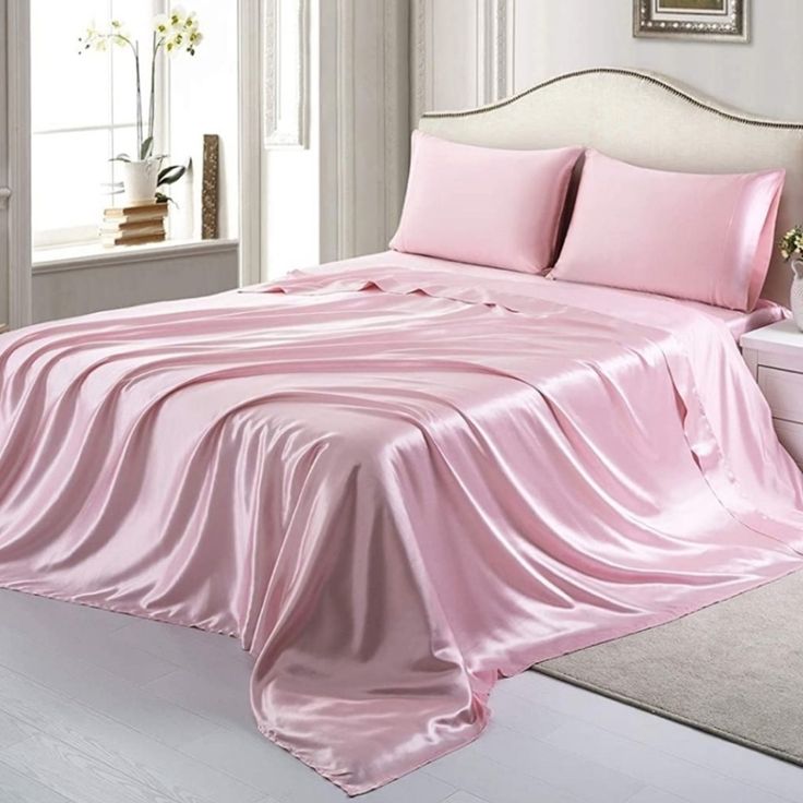 a bed with pink sheets and pillows in a white room next to a window,