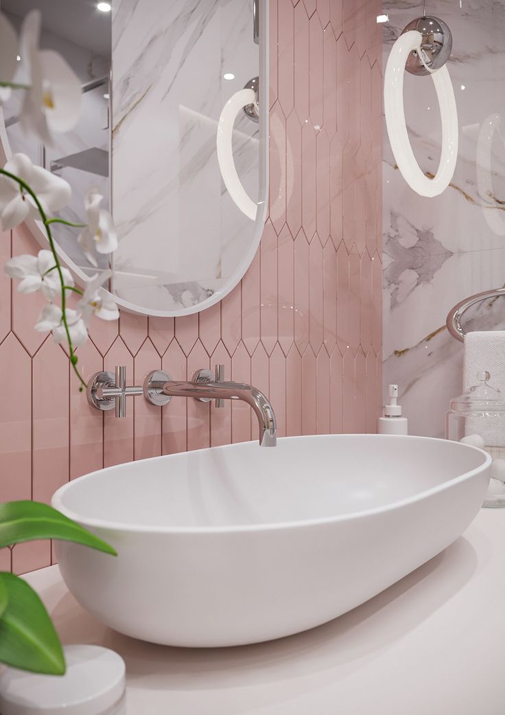 a white sink sitting next to a mirror in a pink tiled bathroom with flowers on the counter