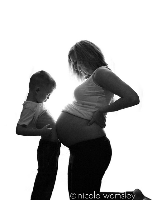 black and white photograph of a pregnant woman holding her baby bumping the belly of a toddler