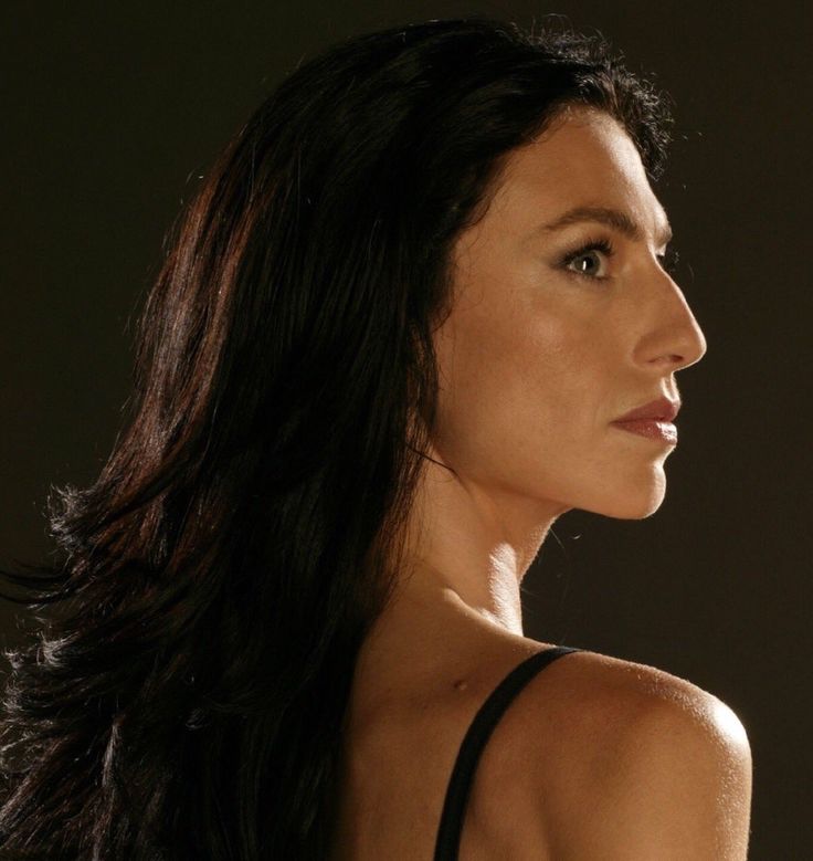 a woman with long dark hair wearing a black top and looking off to the side