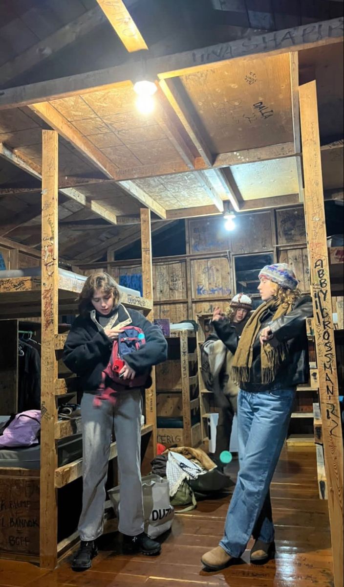 two women are standing in a room with bunk beds and other items on the floor