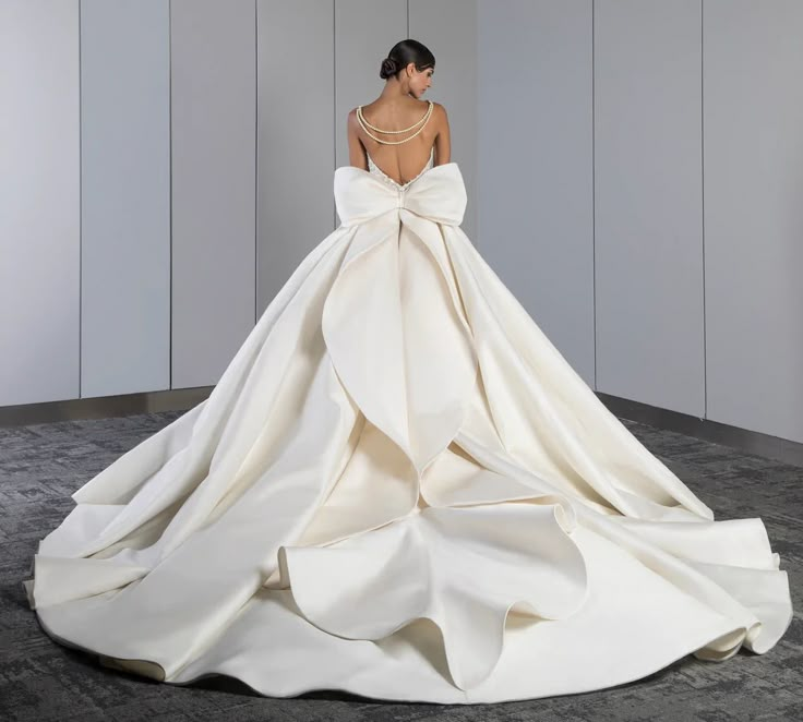 a woman in a white wedding dress with a big bow on her back, looking down at the floor