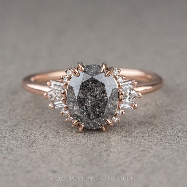 an oval gray diamond surrounded by smaller white diamonds in a rose gold band, on a grey background