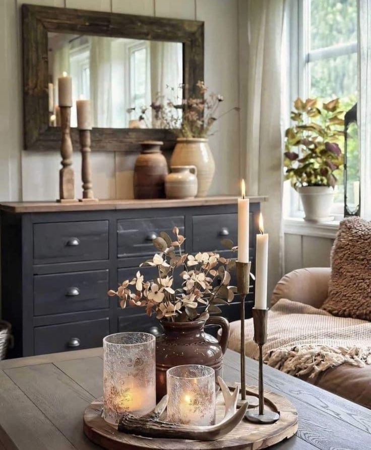 a table with candles and flowers on it in front of a mirror, couch and coffee table