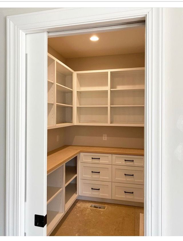 an empty walk in closet with white cabinets and drawers on the bottom shelf is open