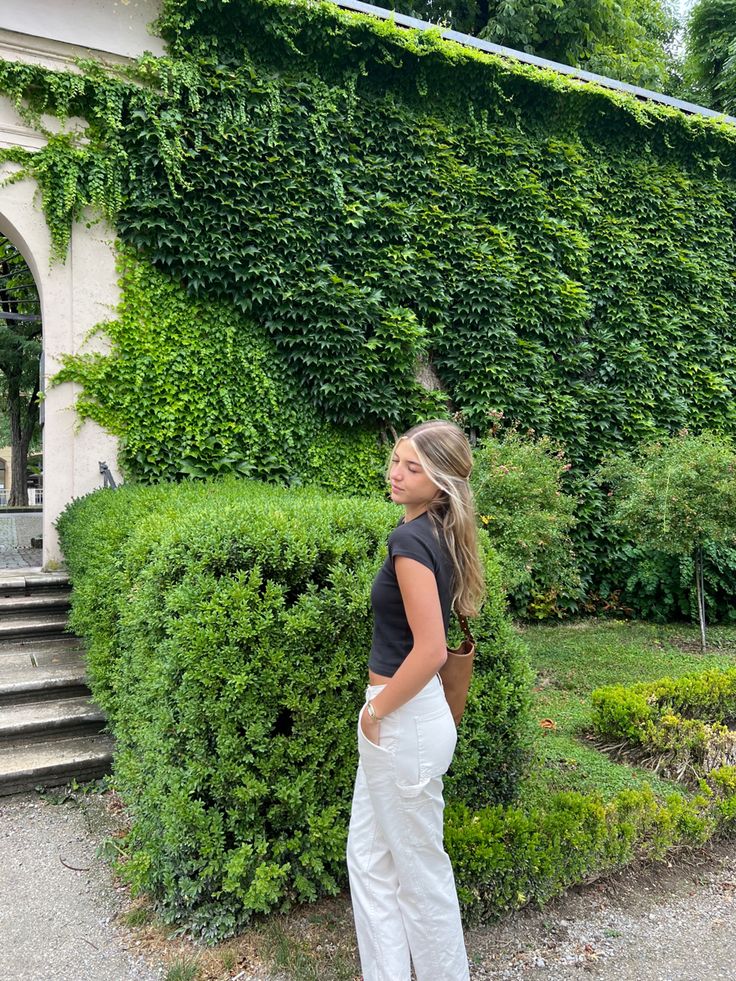 a woman standing in front of a lush green hedge