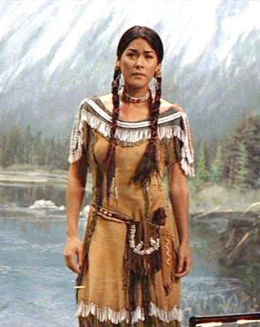 a native american woman standing in front of a mountain lake with her hands on her hips