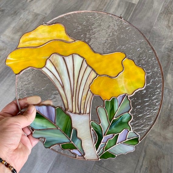 a hand holding up a stained glass plate with a yellow flower on it and leaves