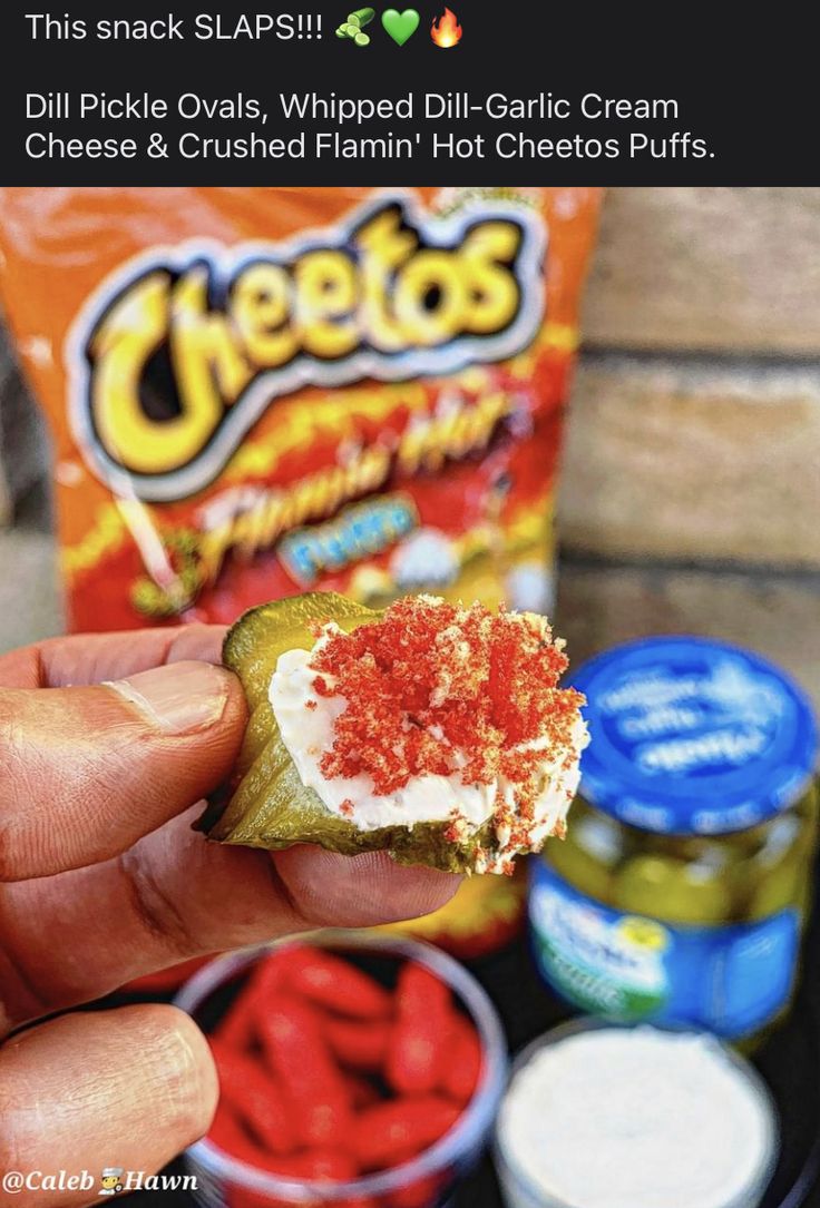 someone is holding up a cracker with cheese and chili on it, next to other snacks