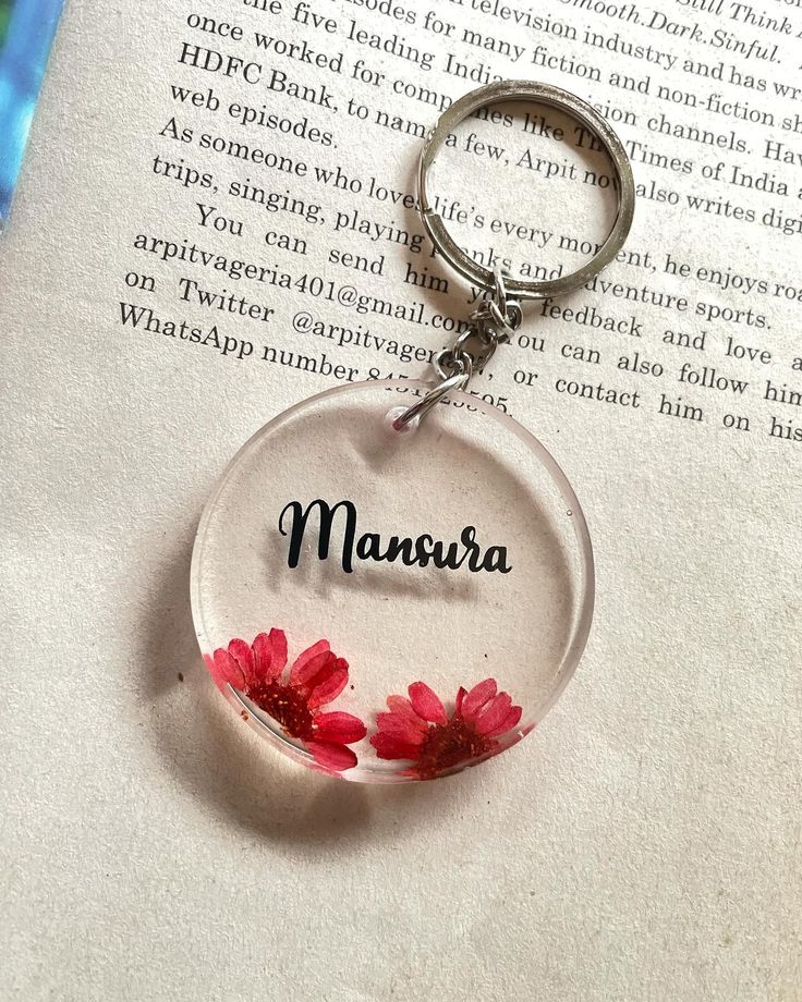 a glass keychain with two red flowers on it and the word maura written in black