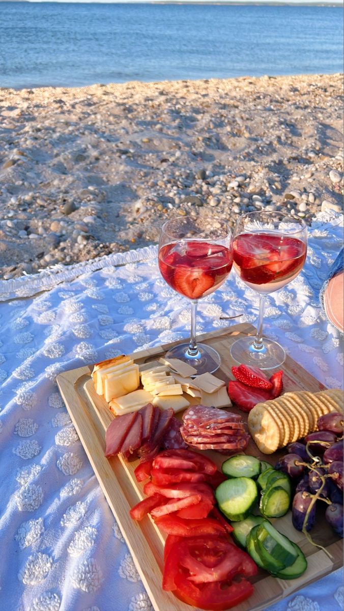 two glasses of wine and some food on a table at the beach with water in the background