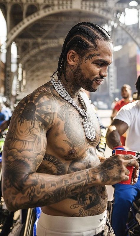 a man with many tattoos on his chest holding a drink and looking at his cell phone