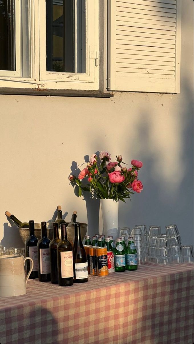 a table topped with lots of bottles and wine glasses next to a window filled with flowers