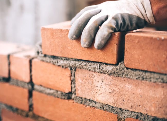 a brick wall being built with gloves on it's arms and hands resting on the bricks