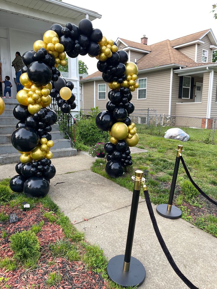 a black and gold balloon arch in front of a house