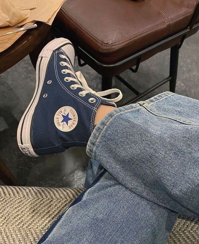 a person sitting on a chair with their feet up and wearing blue converse shoes,