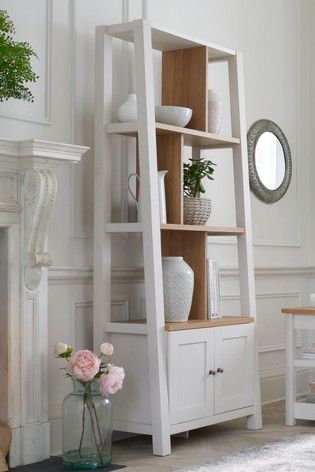 a white bookcase with flowers and vases on it next to a fireplace in a living room