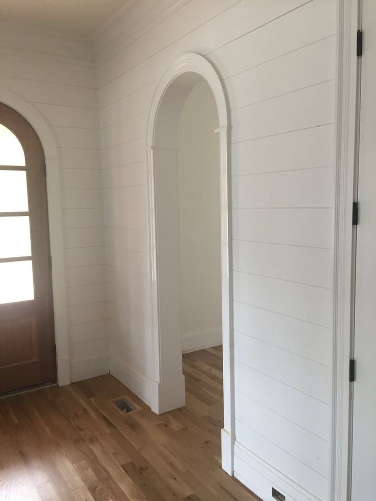 an empty room with white walls and wood flooring, arched doorway leading into another room