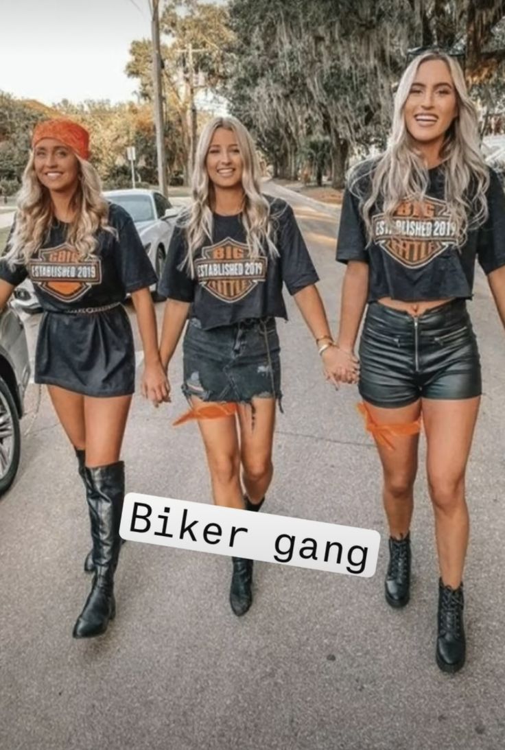 three women walking down the street wearing biker gang t - shirts and leather short shorts