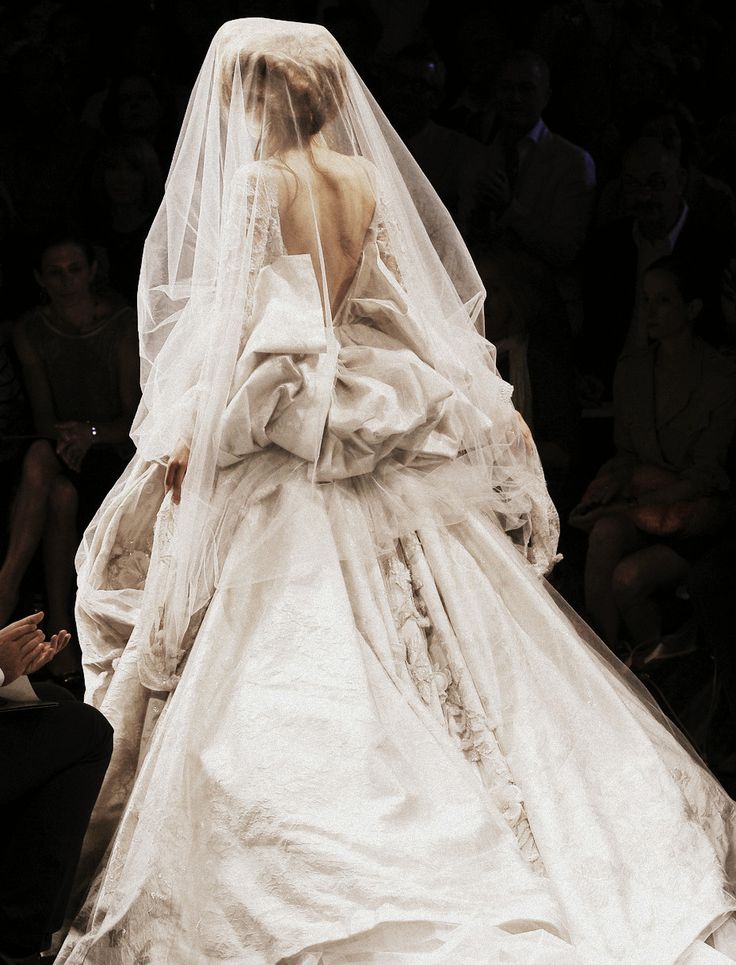 a woman in a white wedding dress walking down the runway with a veil on her head