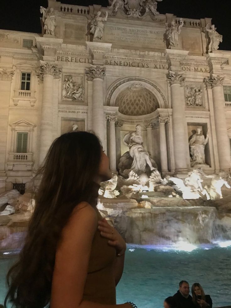 a woman standing in front of a fountain at night