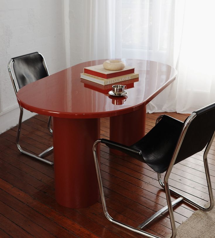 a red table with two black chairs next to it and a stack of books on top