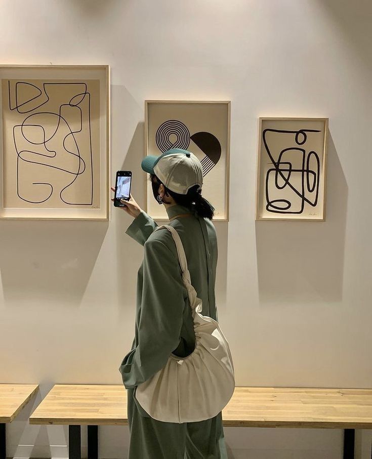 a woman is looking at artwork on the wall with her cell phone in front of her