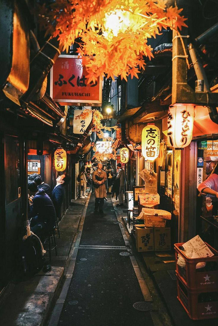 a man is walking down an alley way at night with lanterns hanging from the ceiling