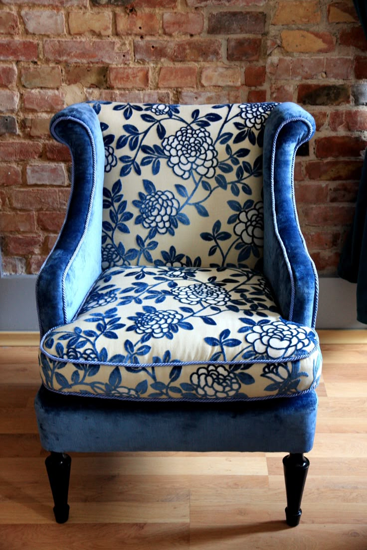 a blue and white chair sitting on top of a hard wood floor next to a brick wall