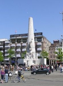 a group of people standing in front of a tall white obelisk on a city street