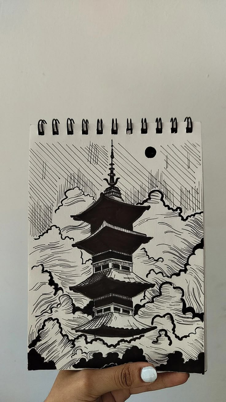 a hand holding up a notebook with an image of a pagoda in the sky on it