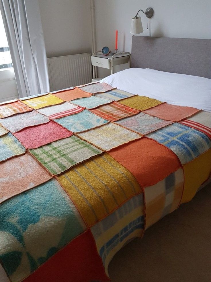 a bed with a colorful blanket on top of it next to a nightstand and window