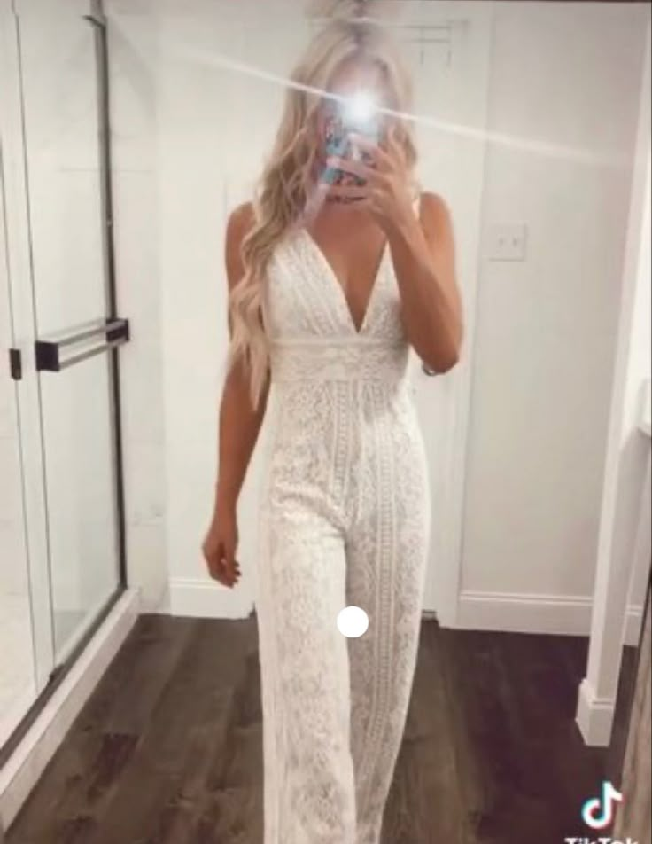 a woman taking a selfie in front of a mirror wearing a white jumpsuit