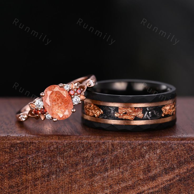 two wedding bands with an orange stone in the center on top of a wooden table